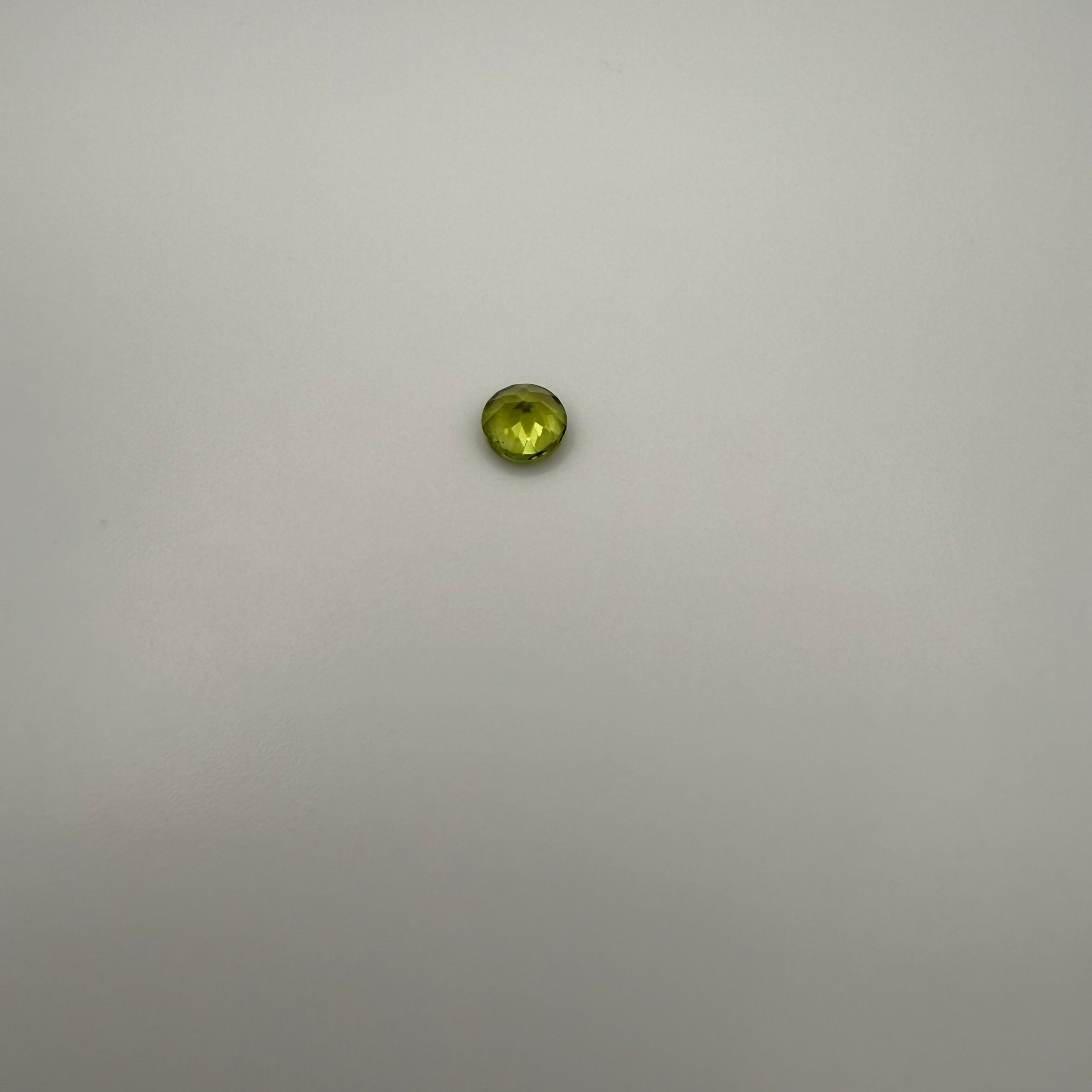round faceted 0.5ct yellow-green peridot gemstone on a light background