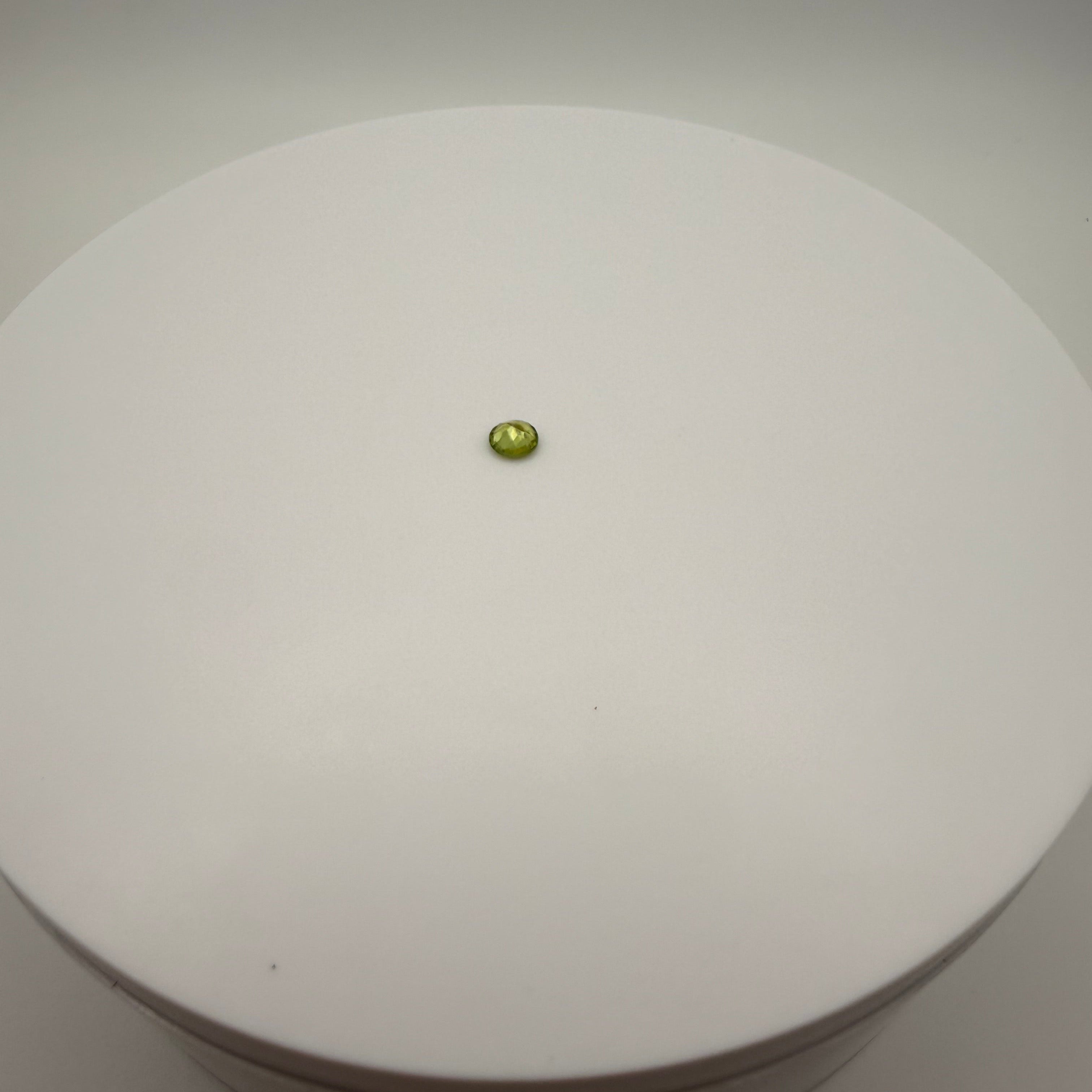 Round faceted 0.45ct yellow-green peridot gemstone centered on a white circular surface