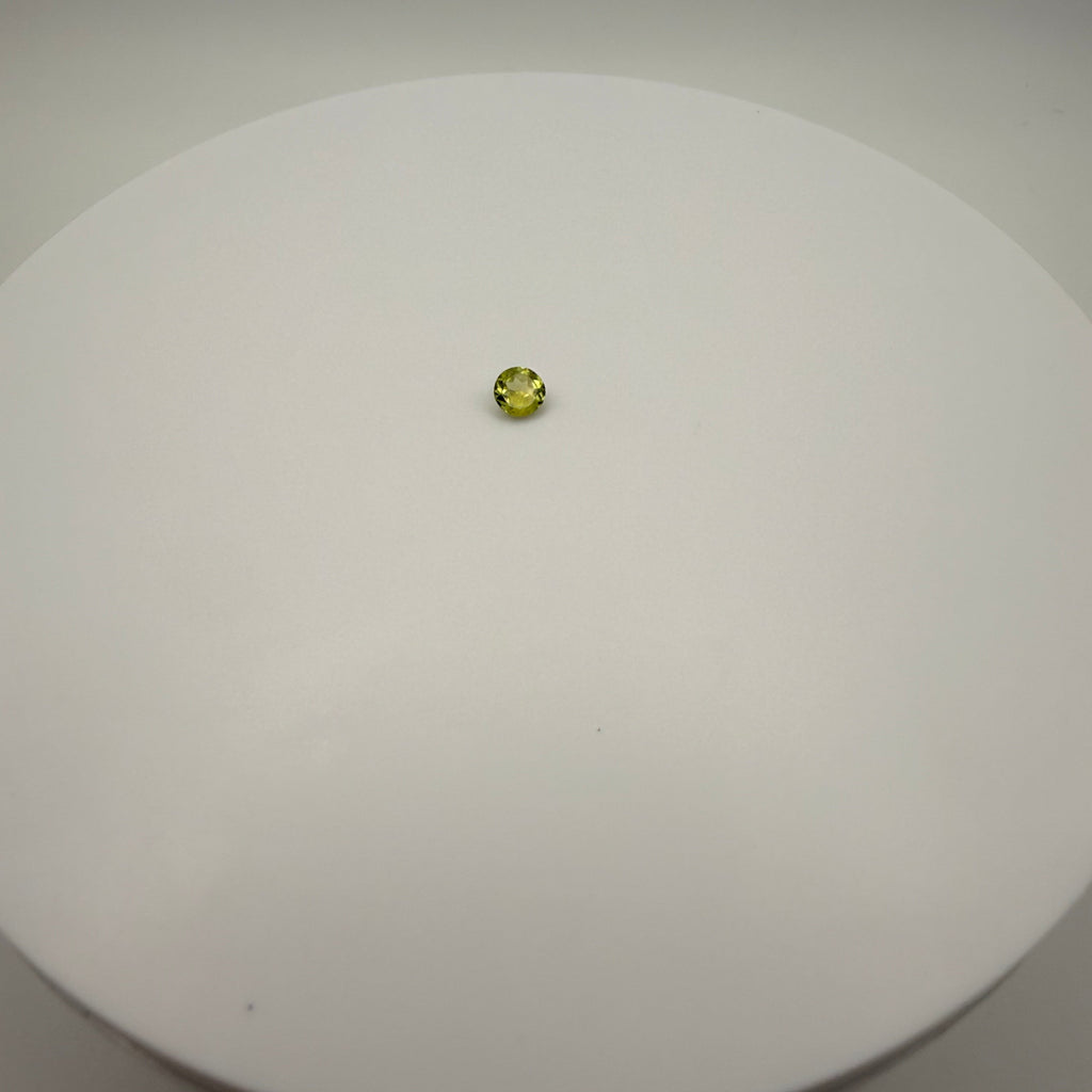 0.45ct yellow-green peridot round faceted gemstone centered on a white circular surface
