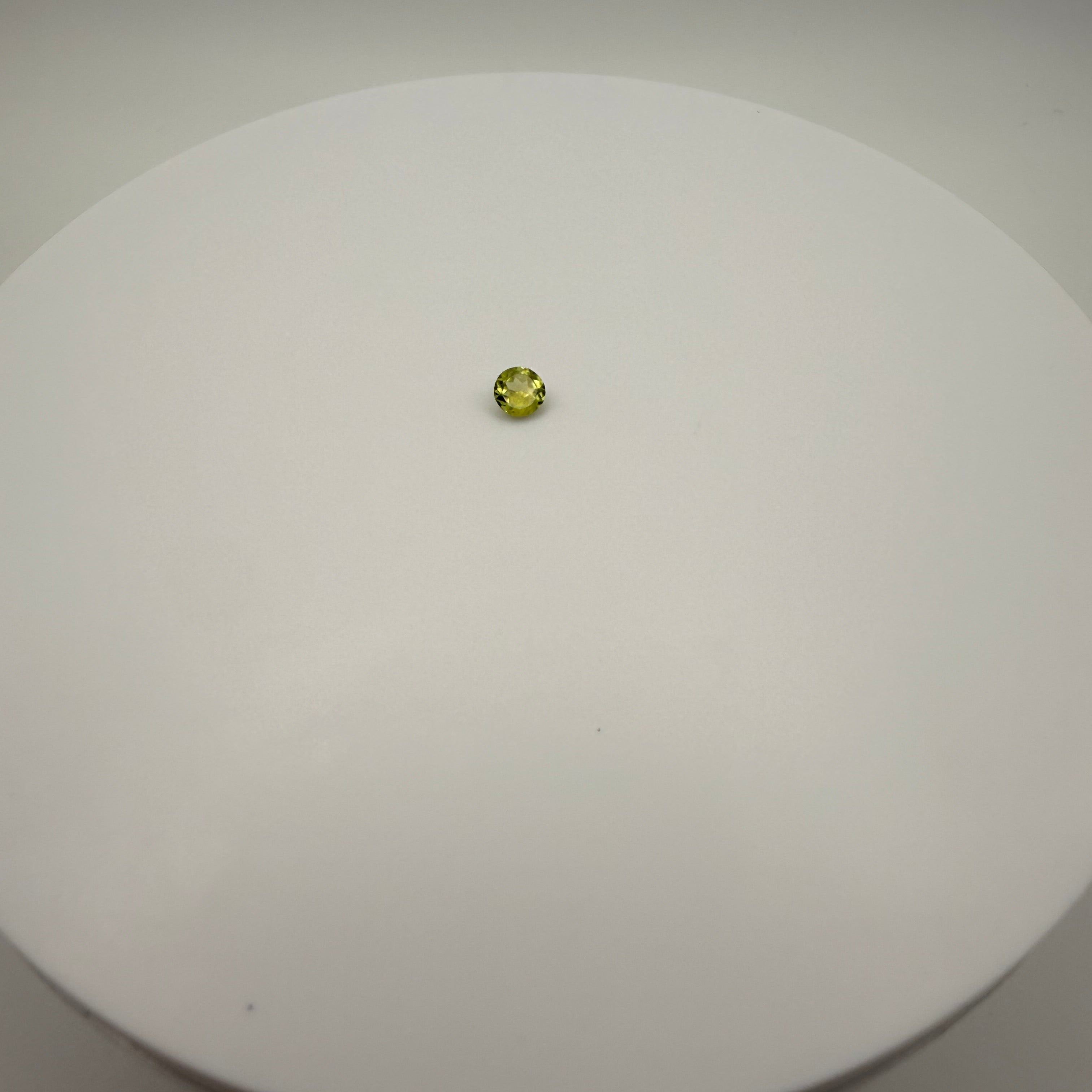 0.45ct yellow-green peridot round faceted gemstone centered on a white circular surface