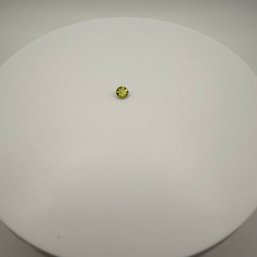 0.45ct yellow-green peridot round faceted gemstone centered on a white circular surface