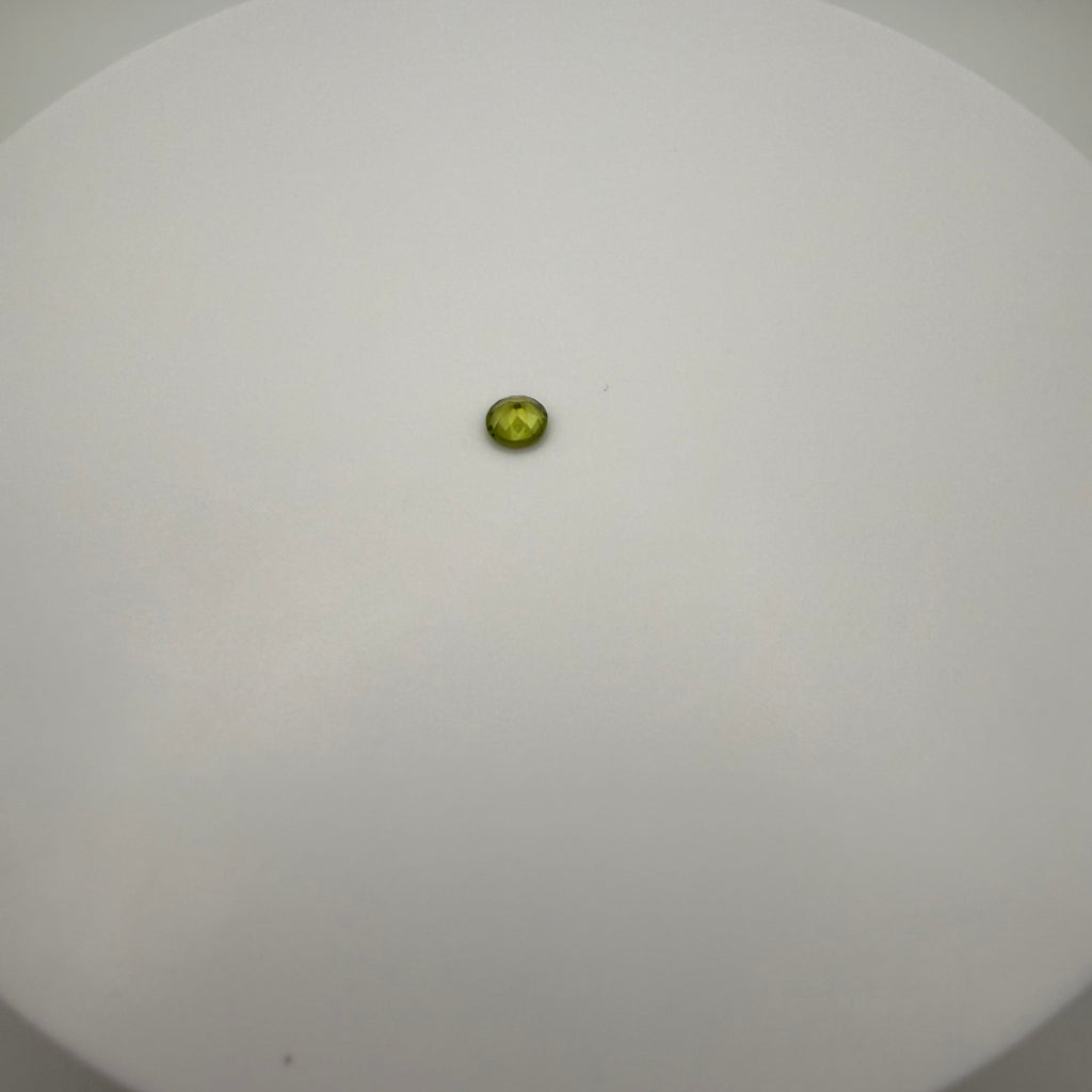 macro view of 0.5ct yellow-green peridot round faceted gemstone on a smooth white surface