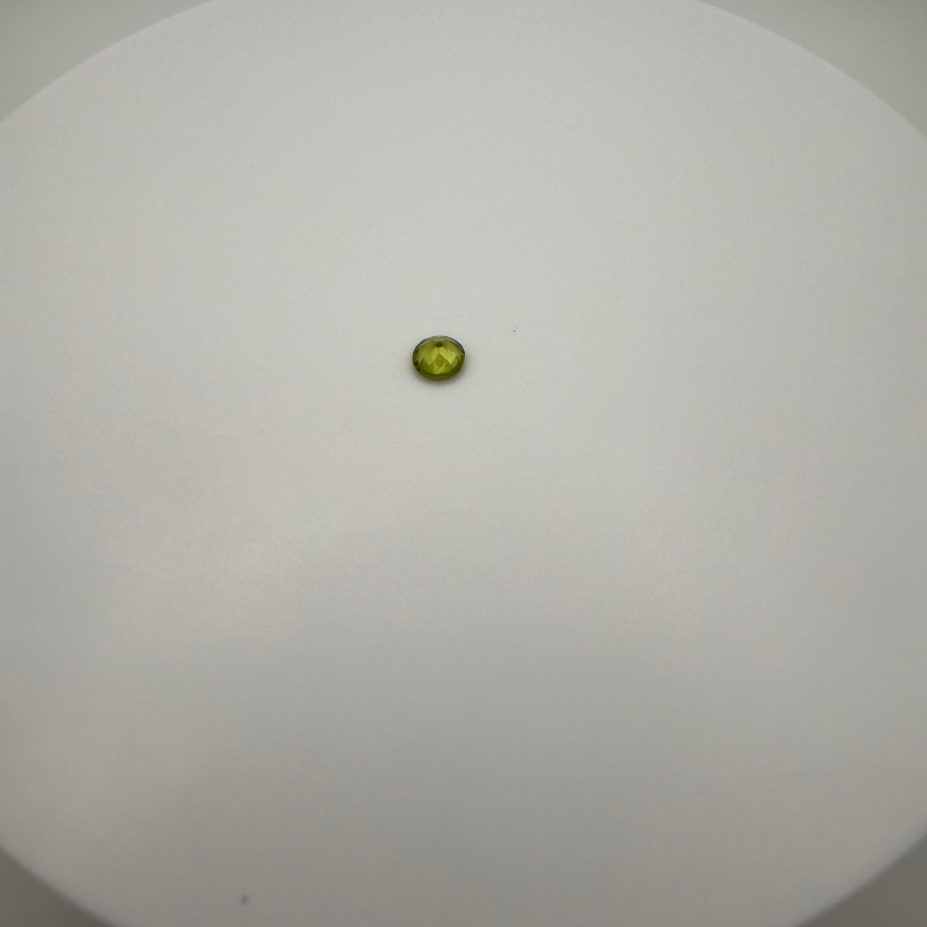 macro view of 0.5ct yellow-green peridot round faceted gemstone on a smooth white surface