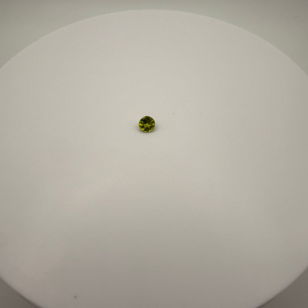 Round faceted 0.5ct yellow-green peridot gemstone on a white display surface