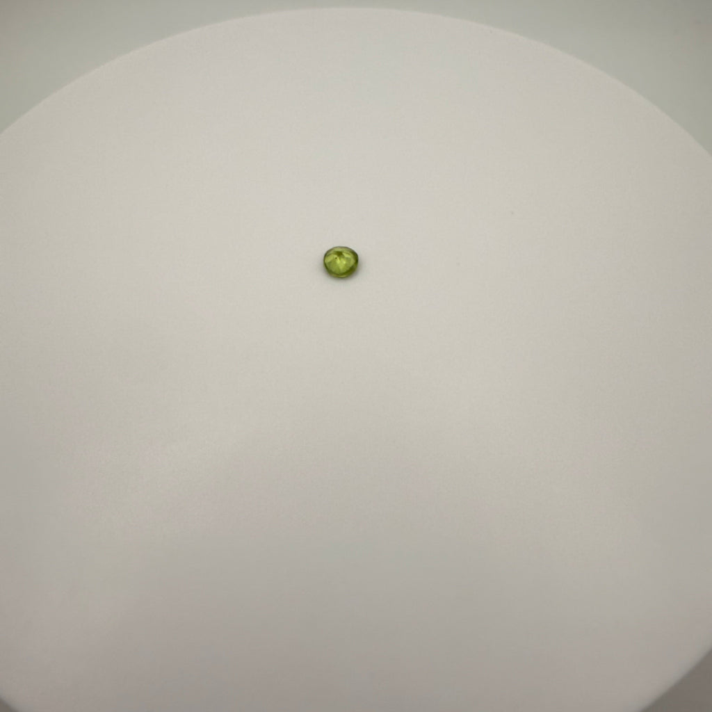 macro top down view of 0.45ct yellow-green peridot round faceted gemstone on a smooth white surface