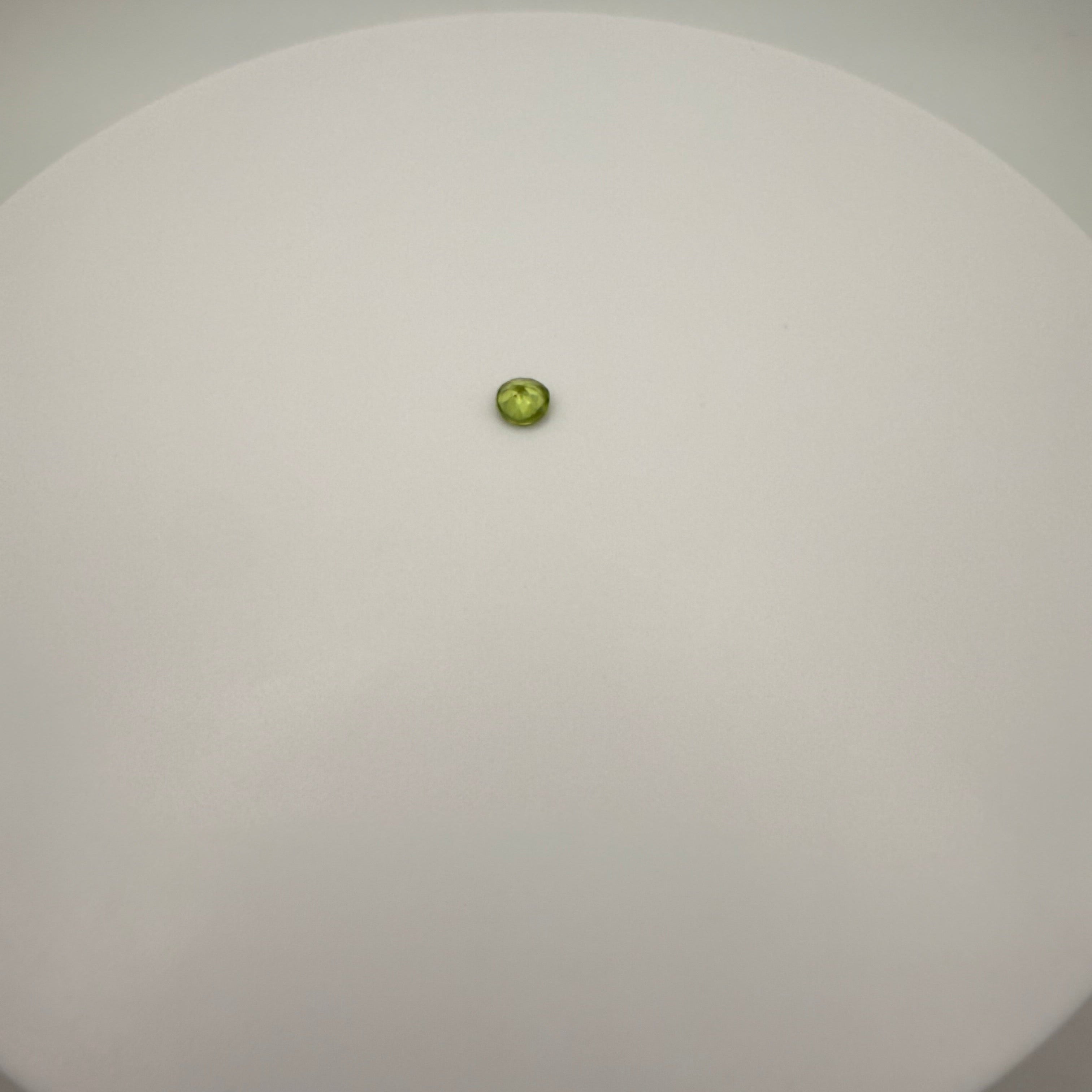 macro top down view of 0.45ct yellow-green peridot round faceted gemstone on a smooth white surface