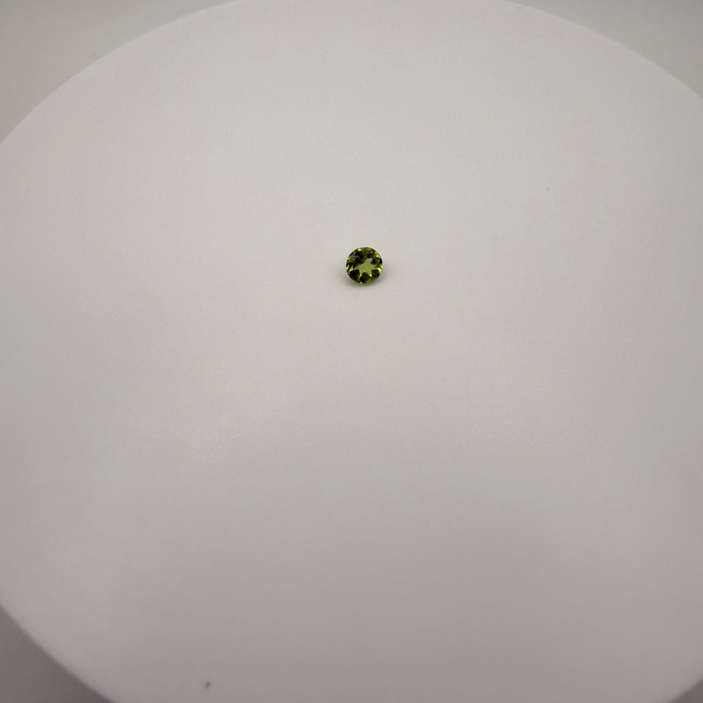 Round faceted 0.45ct yellow-green peridot gemstone centered on a smooth white surface
