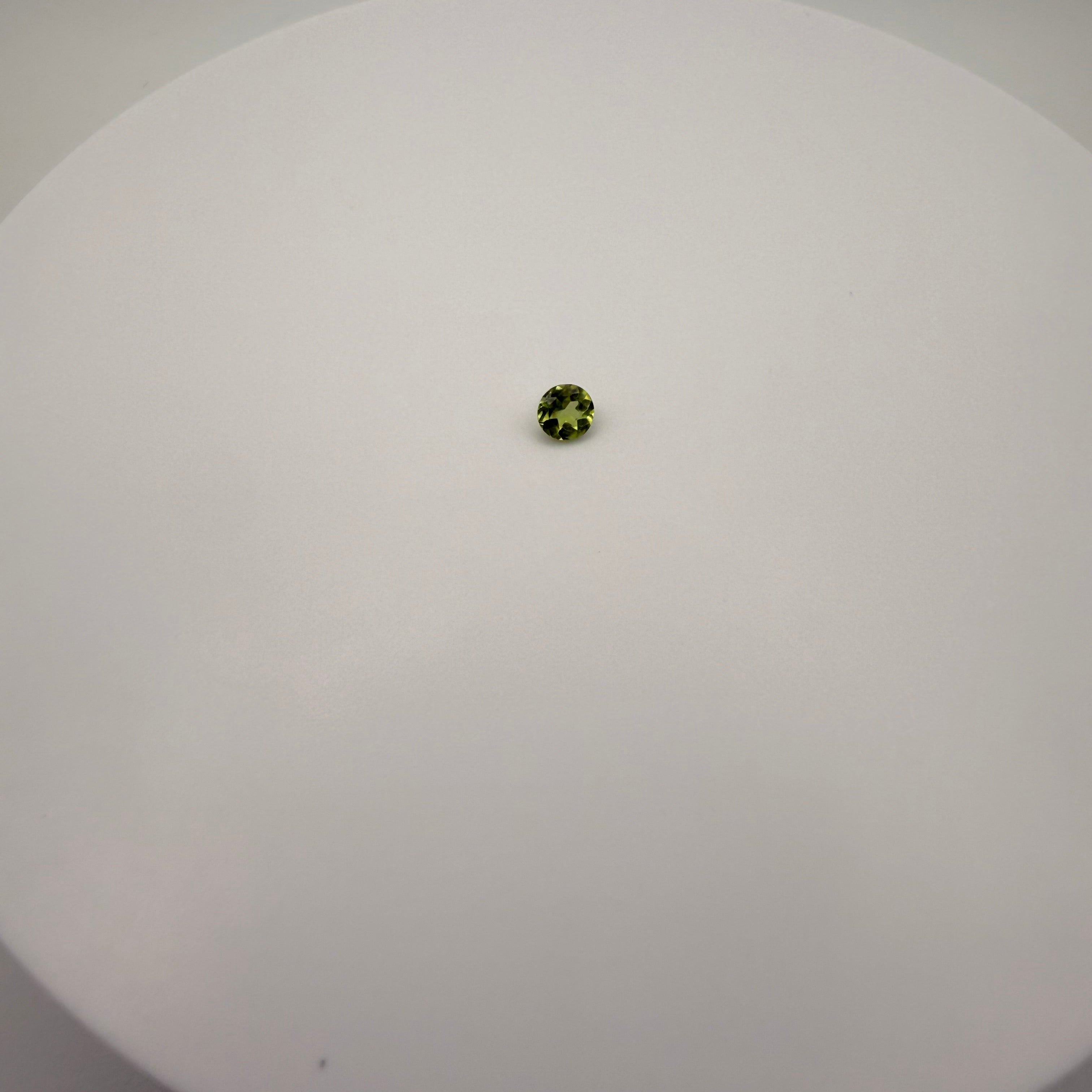 Round faceted 0.45ct yellow-green peridot gemstone centered on a smooth white surface