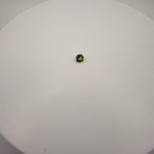 Round faceted 0.45ct yellow-green peridot gemstone centered on a smooth white surface