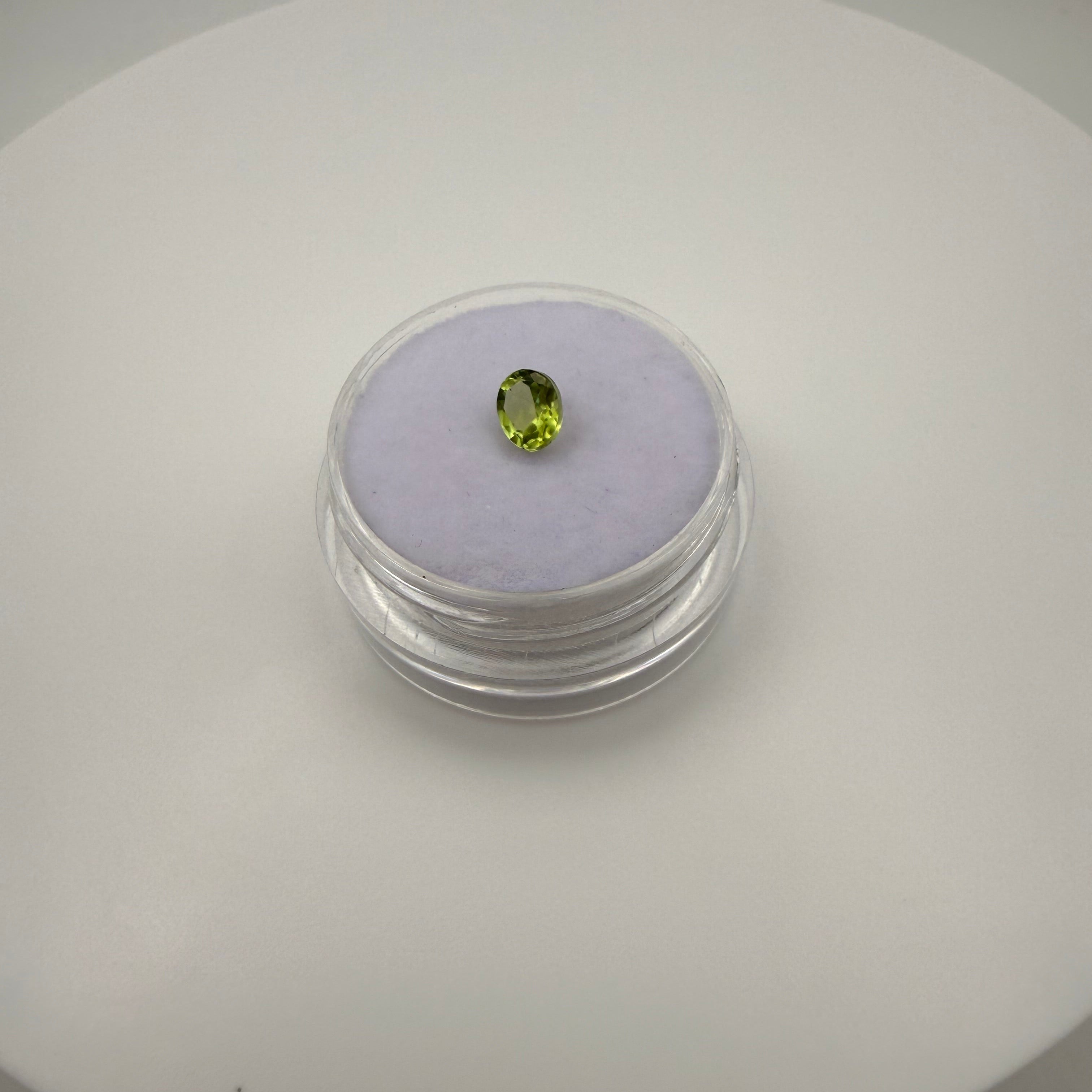 0.45ct oval faceted yellow-green peridot gemstone displayed on a circular white background with a soft purple holder.