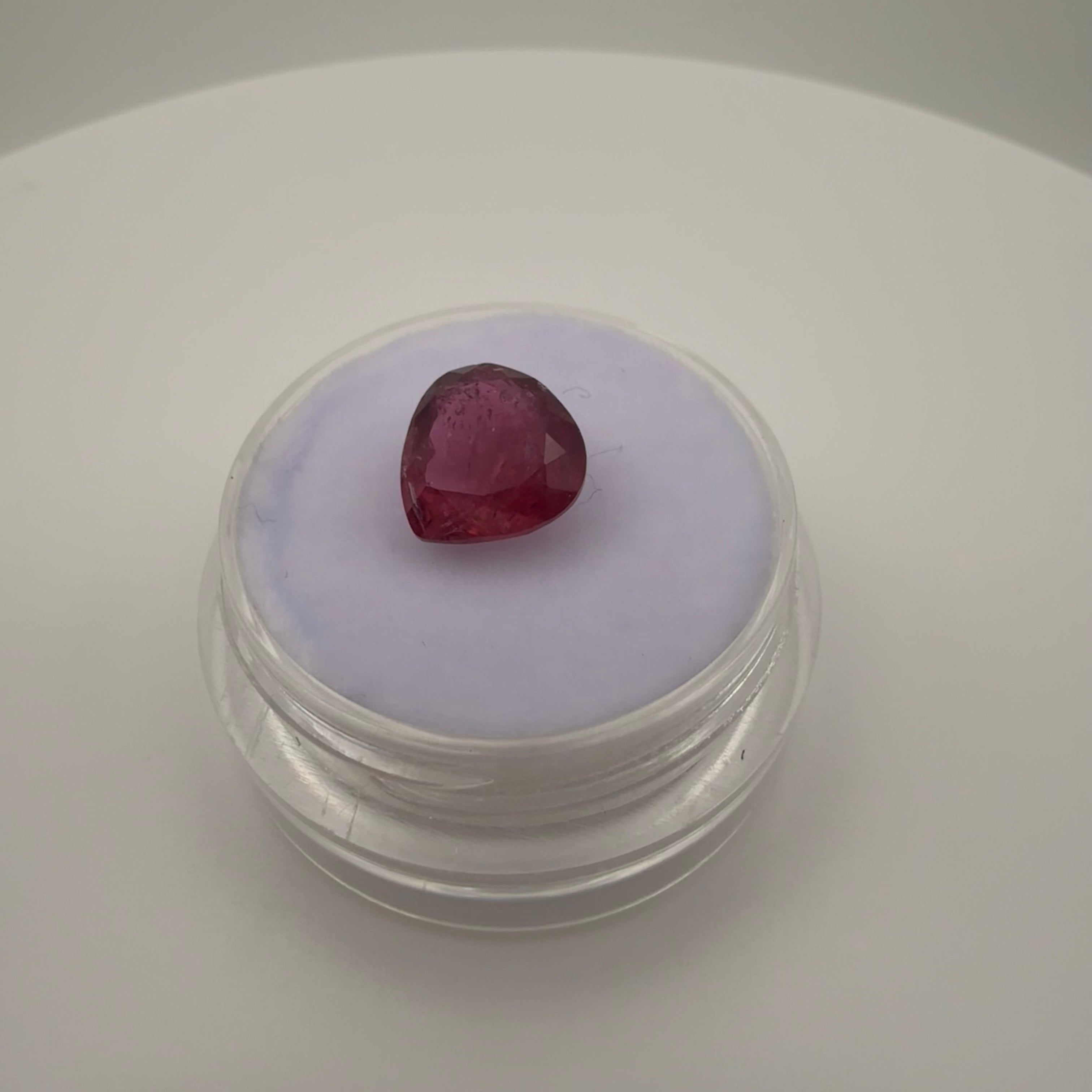 2.1 carat hot pink pear faceted tourmaline sitting on top of a gemstone holder