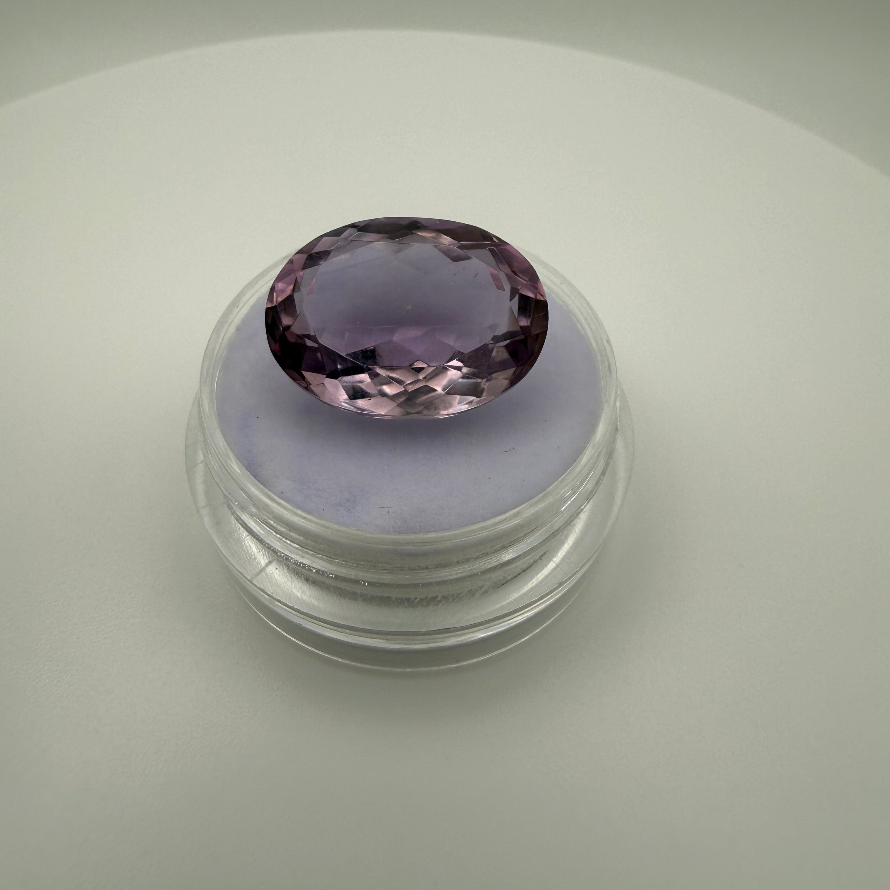 Macro top-down view of a 9.8ct lilac amethyst oval faceted gemstone sitting on a soft purple display holder.