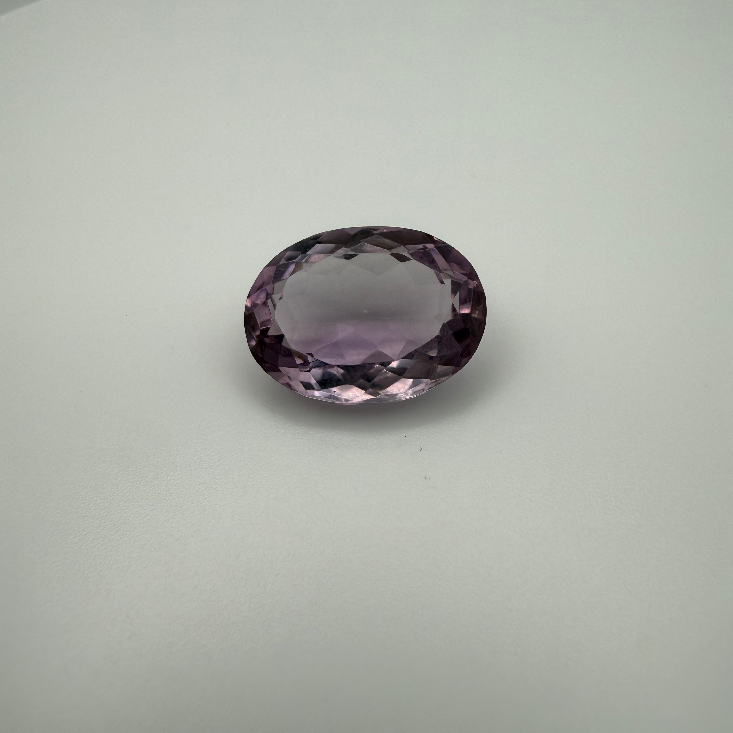 oval faceted lilac amethyst gemstone on a light background