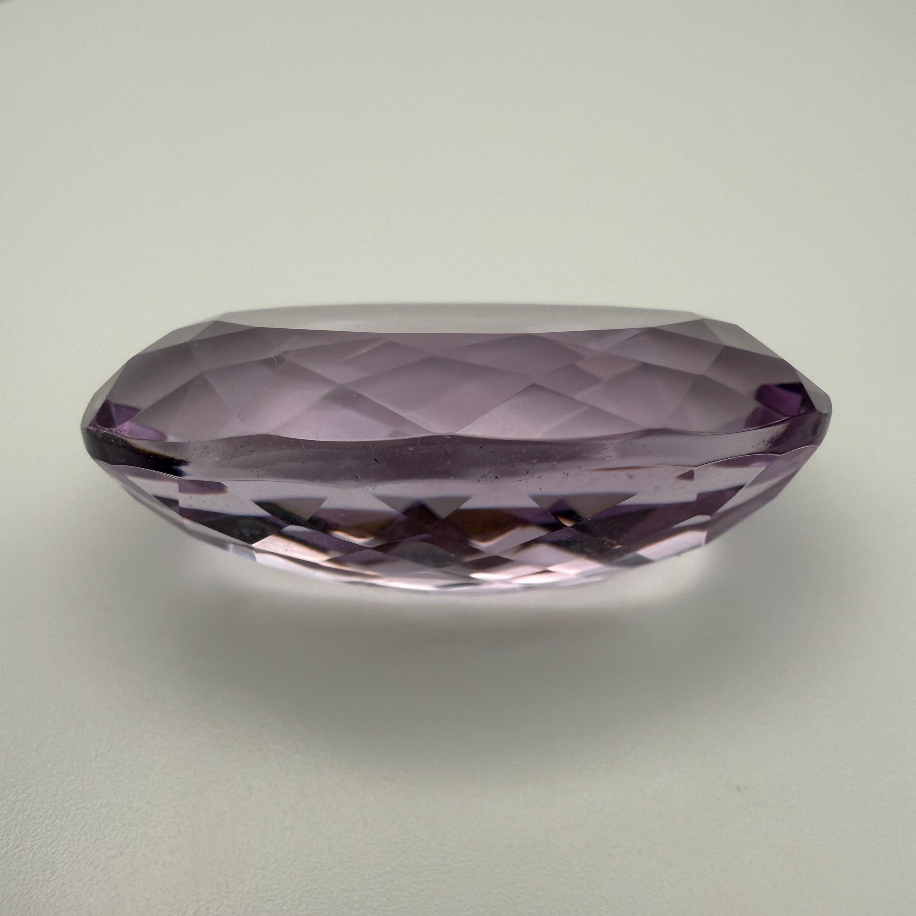 oval faceted 61.6ct Rose de France amethyst gemstone on a light background