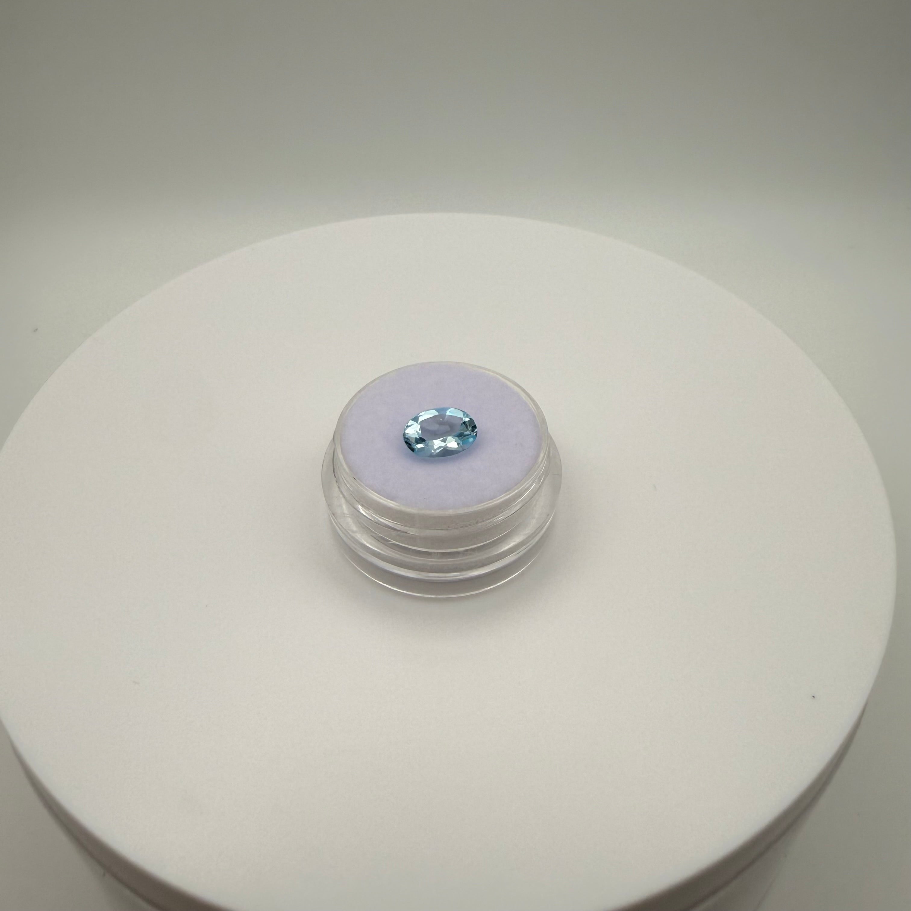 macro top down view of 1.98ct Swiss Blue Topaz oval faceted gemstone on a soft surface in a gem holder against a light background