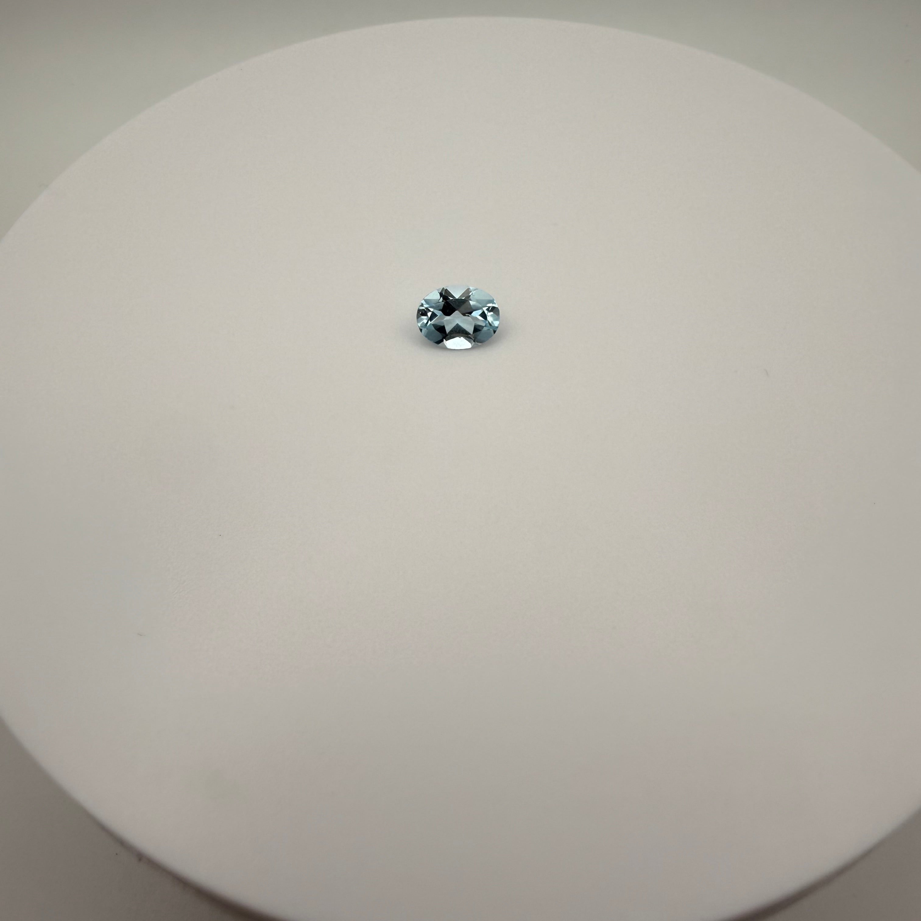 oval faceted 1.95ct Swiss Blue Topaz gemstone on a smooth white circular surface viewed from above